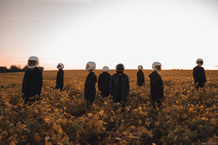 A field of identically dressed figures, faces hidden behind helmets, standing apart from one another at dusk.